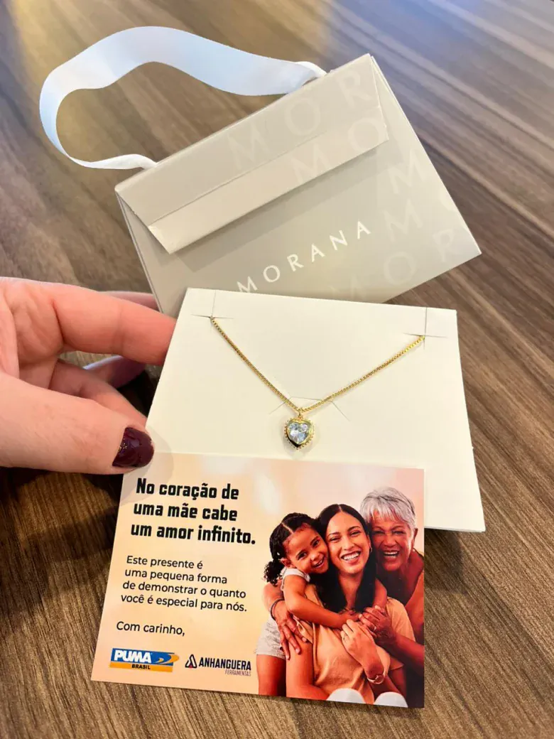 Presente corporativo personalizado da Morana: colar com pingente de coração sobre um cartão de mensagem, acompanhado da sacola da marca.